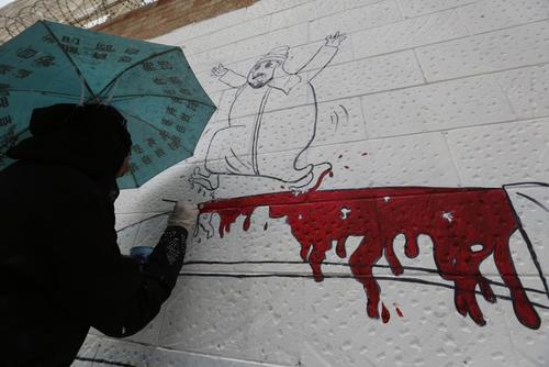 یک هنرمند یمنی مشغول به تصویر کشیدن یک نقاشی به نشانه محکومیت حمله نظامی سعودی ها به یمن بر دیوار ساختمان سفارت عربستان در شهر صنعا