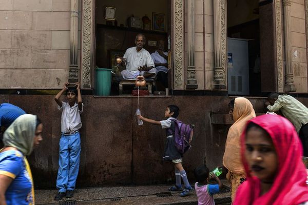 کاهن هندو در حال ریختن آب در ظرف یک کودک مدرسه ای در محله قدیمی دهلی نو