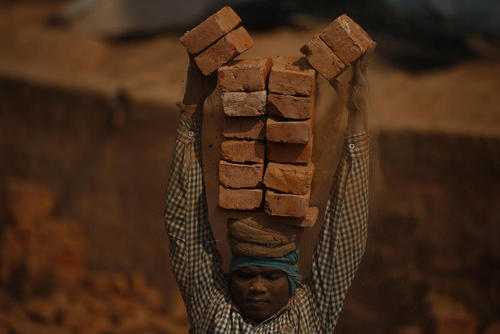یک کارگر مهاجر ساختمانی در حال جابجایی آجر در شهر زلزله زده باختاپور نپال