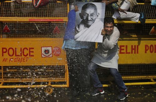 یک تظاهرات کننده حزب کنگره هند تابلوی تصویر مهاتما گاندی رهبر استقلال هند را برای امان ماندن از ماشین آب پاش پلیس هند در مقابل خود گرفته است