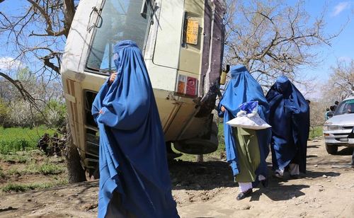 عبور زنان افغان از کنار مینی بوس واژگون شده طی انفجار بمب در کابل افغانستان