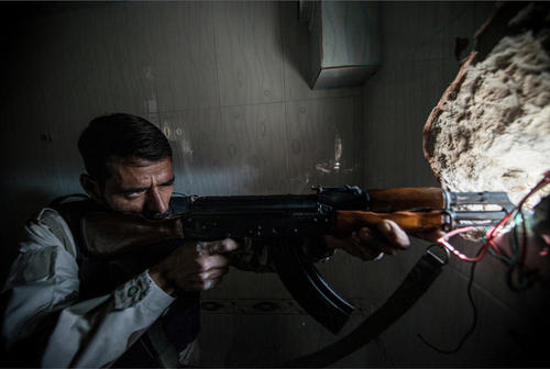 یکی از نیروهای مخالف بشار اسد در حال شلیک به سمت نیروهای دولتی از خانه ای درشهر حلب سوریه 