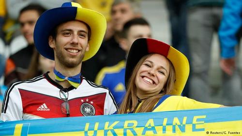 زوجی با دو ملیت متفاوت. مردی با پیراهن تیم ملی آلمان و کلاهی با رنگ‌های پرچم اوکراین و زنی با پیراهن تیم ملی اوکراین و کلاهی با رنگ‌های پرچم آلمان.